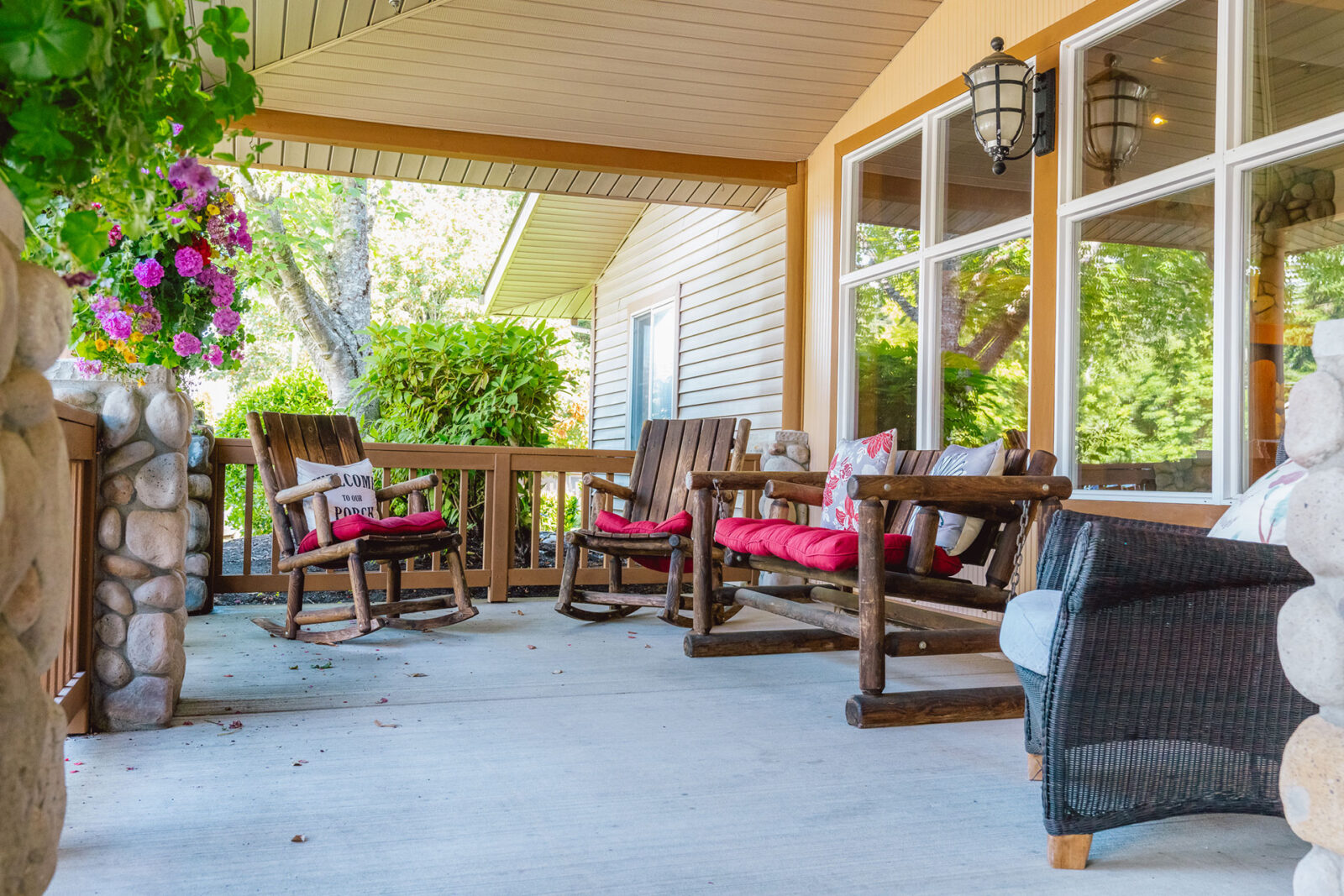 Cozy porch with wooden rocking chairs, colorful flowers, and serene greenery in the background.