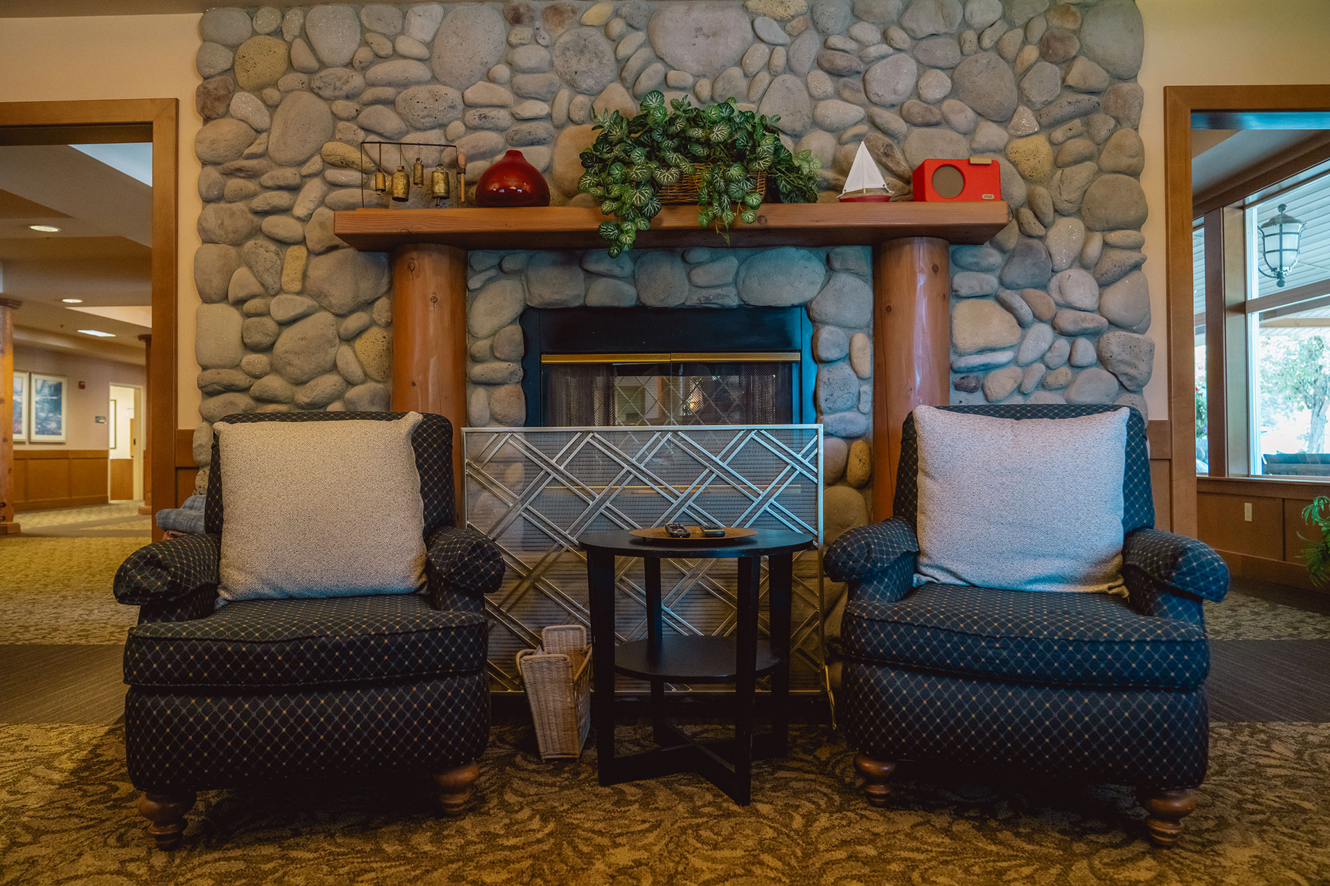 Cozy seating area with two chairs, stone fireplace, and rustic decor on wooden shelves.