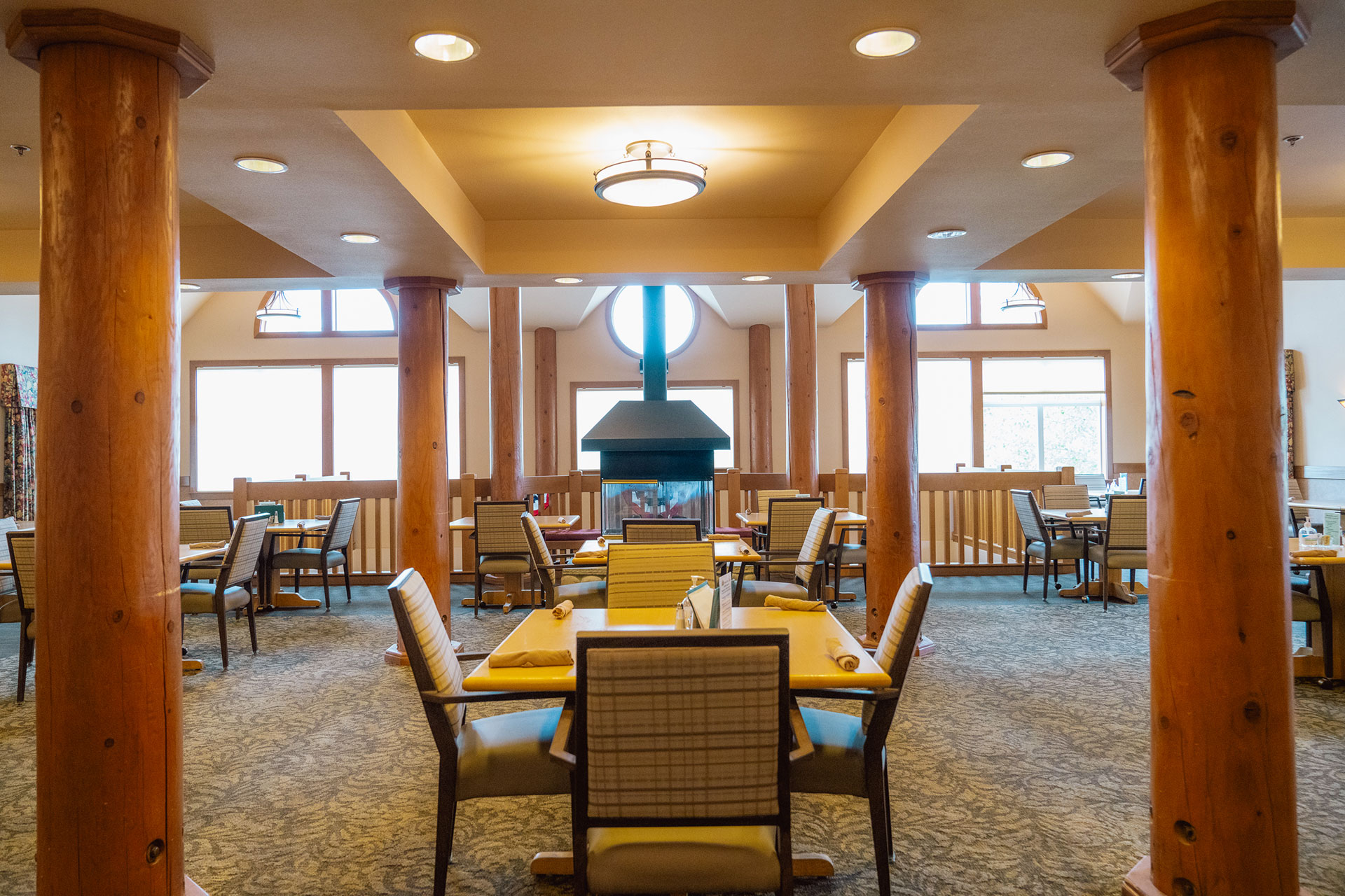 A cozy dining area with wooden pillars, tables, and a central fireplace.