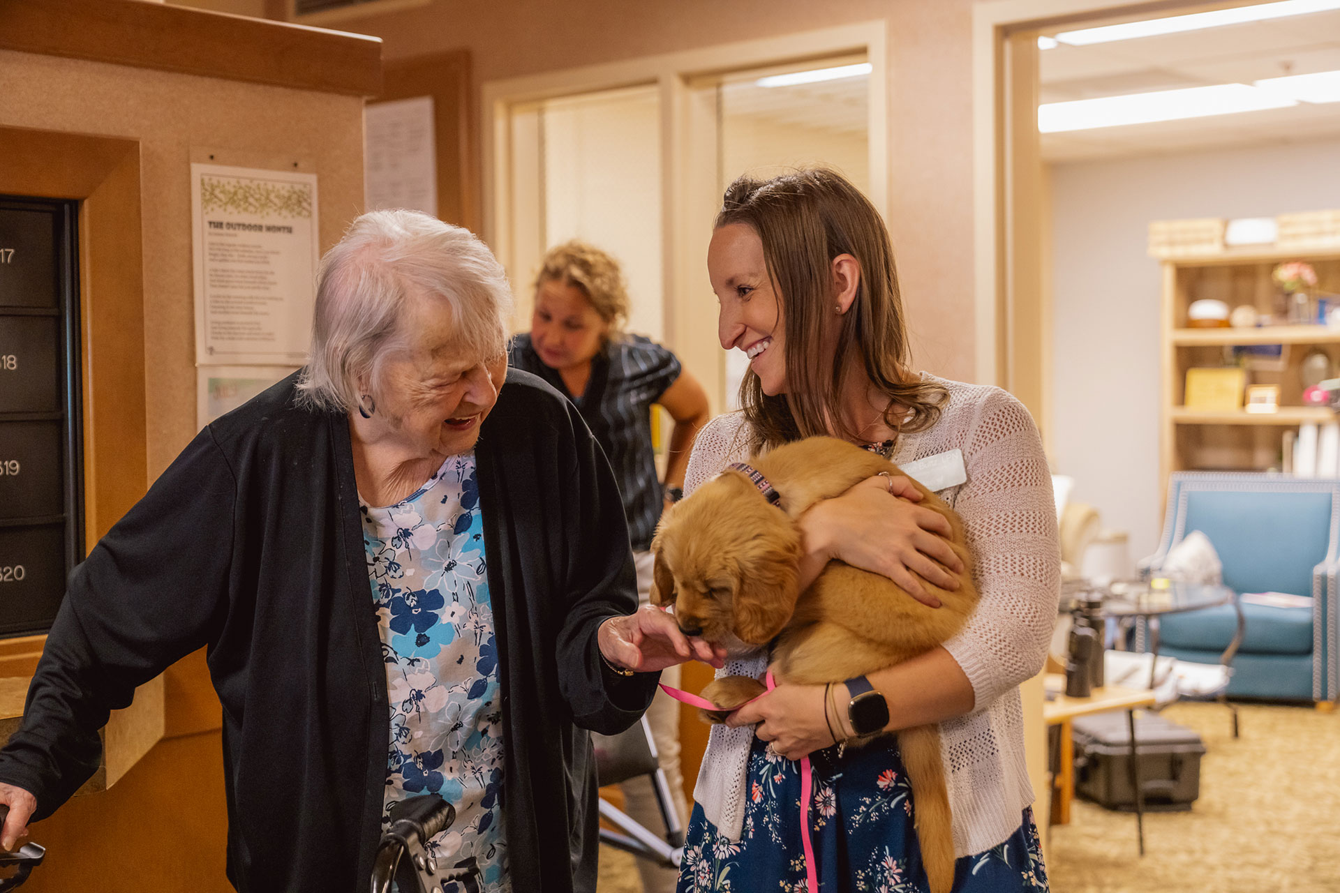 A joyful interaction between an elderly woman and a caregiver holding a puppy.